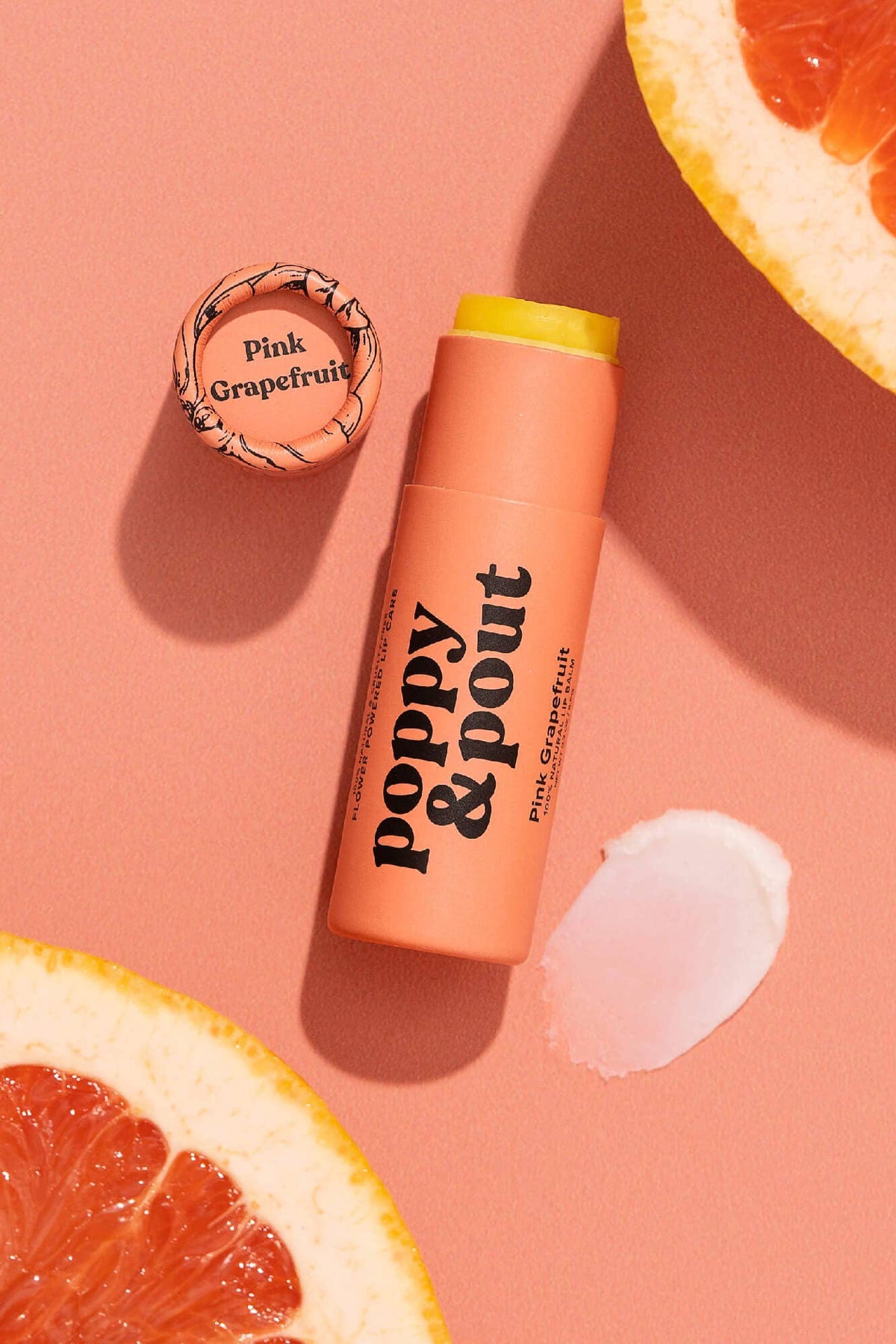Lip balm with 'Poppy & Pout' branding on a pink background with grapefruit slices.
