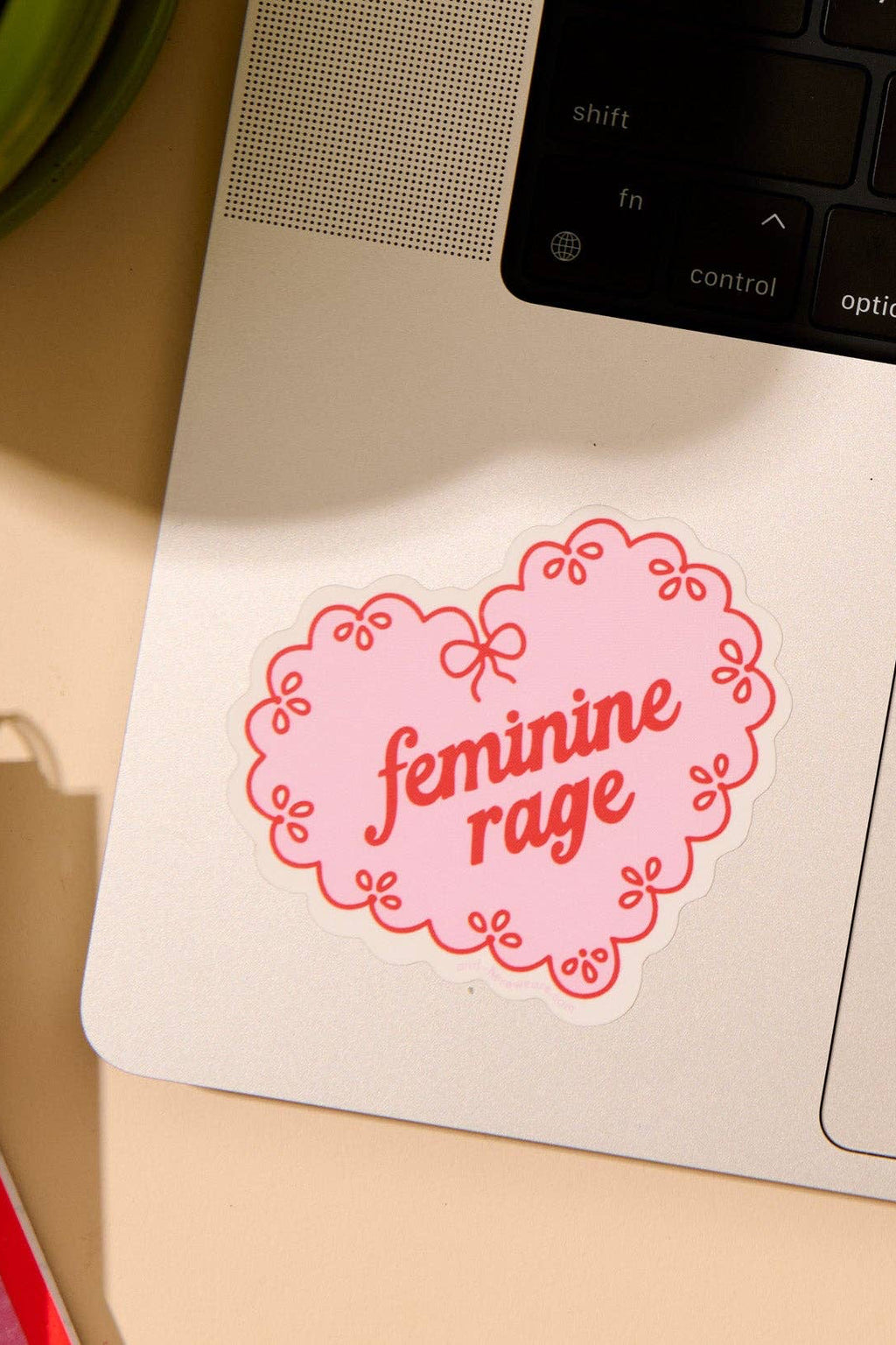 Laptop with a 'feminine rage' sticker on a desk with a notebook and plant.