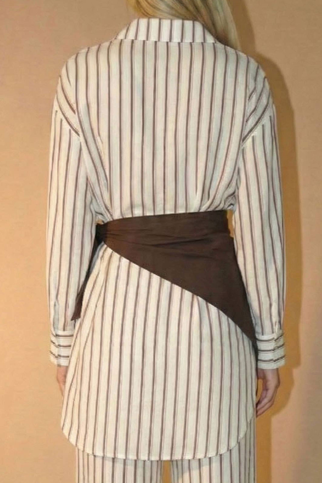 Person wearing a striped top with a brown scarf against a beige background