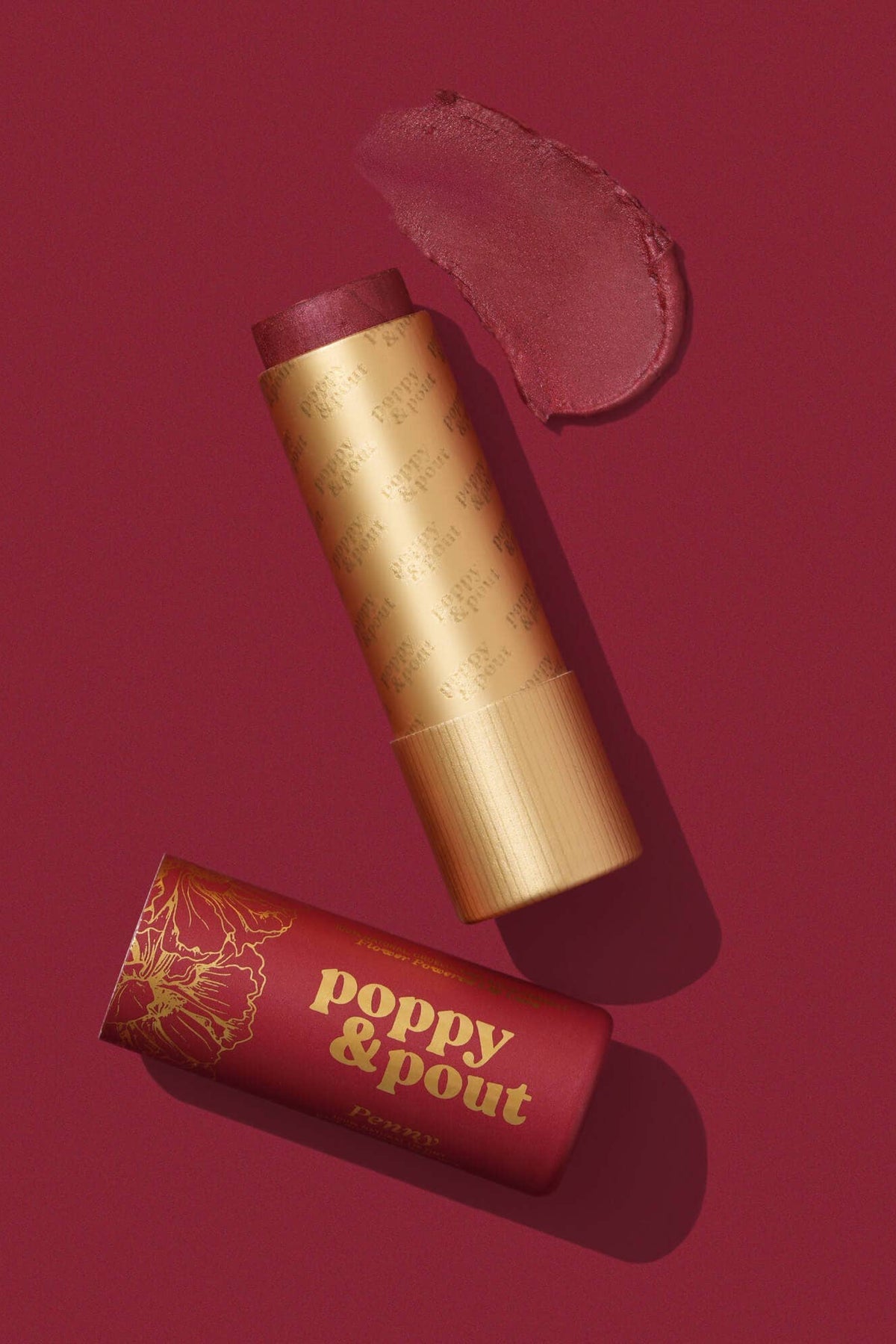 Lip balm with gold tube and red container labeled 'poppy & pout' on a red background