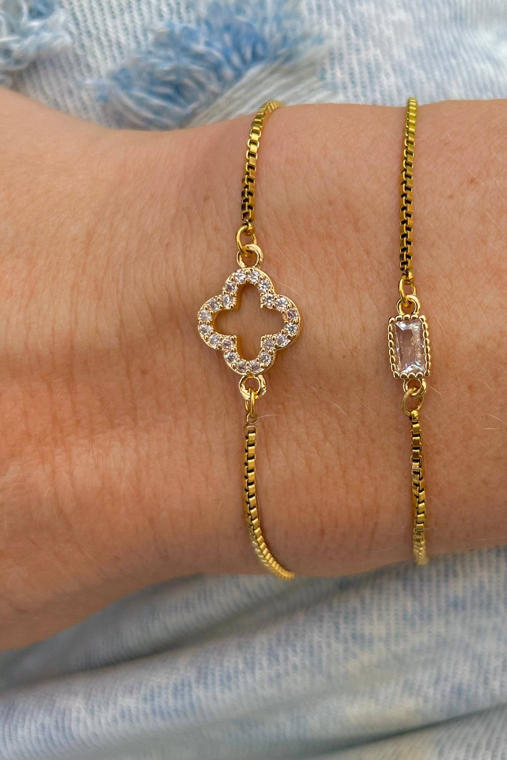 Gold bracelets with diamond and gemstone designs on a wrist against a denim background