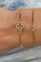 Gold bracelets with diamond and gemstone designs on a wrist against a denim background