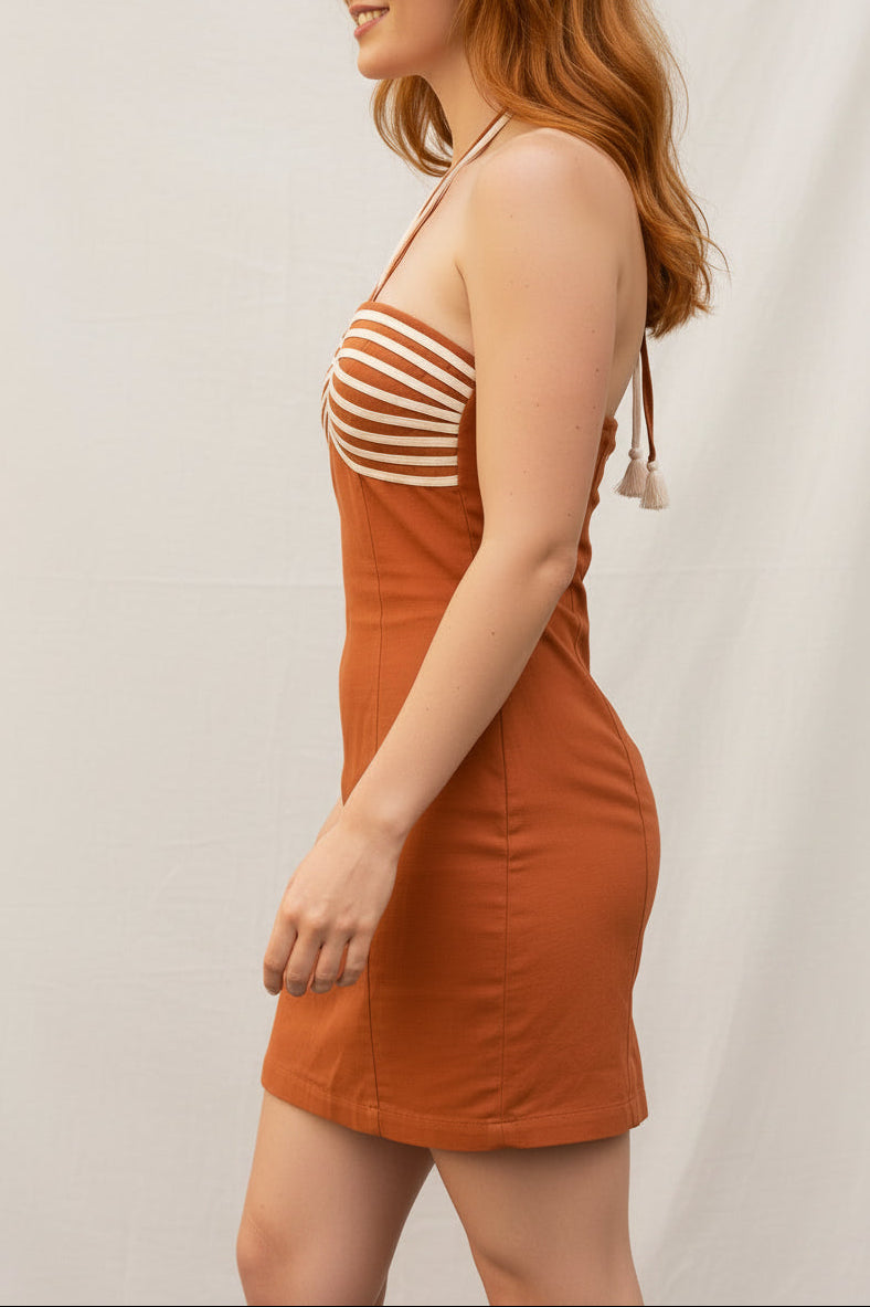 A woman with red hair wearing a terracotta orange strapless mini dress with white horizontal stripes on the bust walks through an outdoor cafe setting.