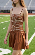 A young woman walks across a green football field wearing a brown mini dress with a geometric pattern, white sneakers, and standing next to the number 30.