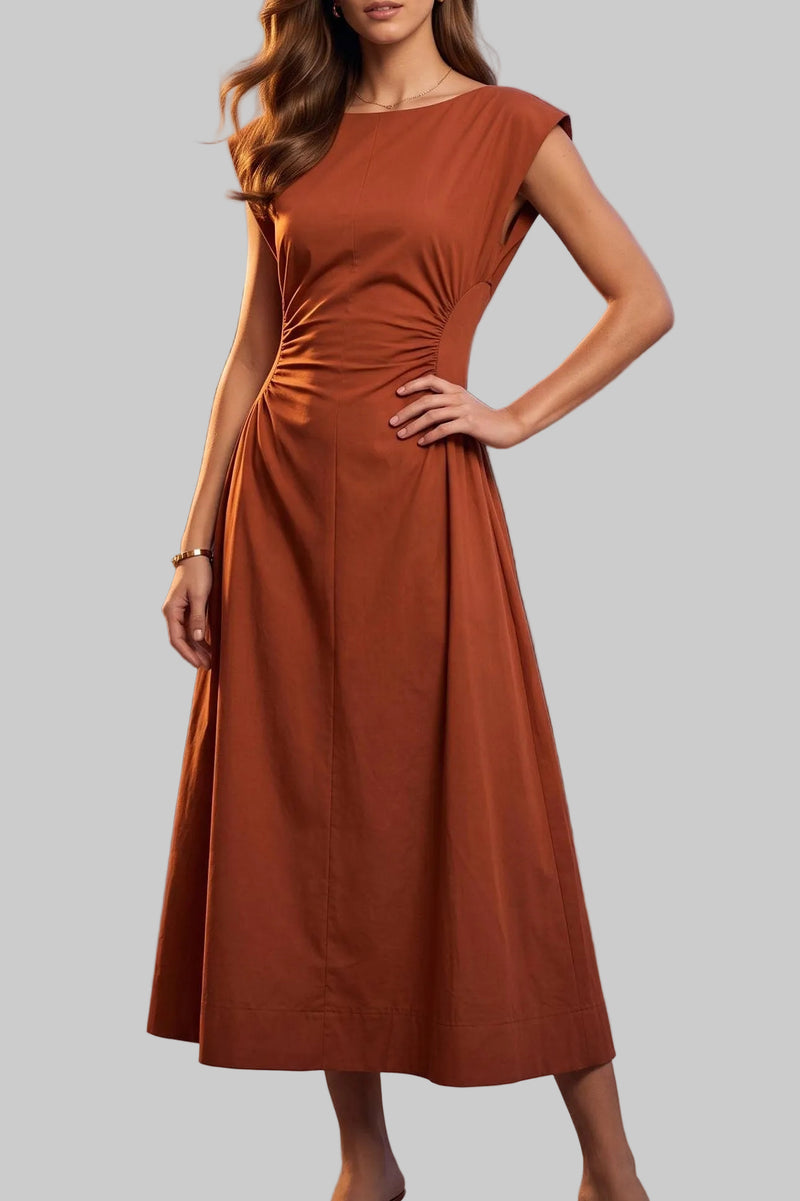 A woman stands on an outdoor terrace at dusk wearing a rust-orange midi dress with cap sleeves and a gathered waist. Guests and string lights are visible in the background.