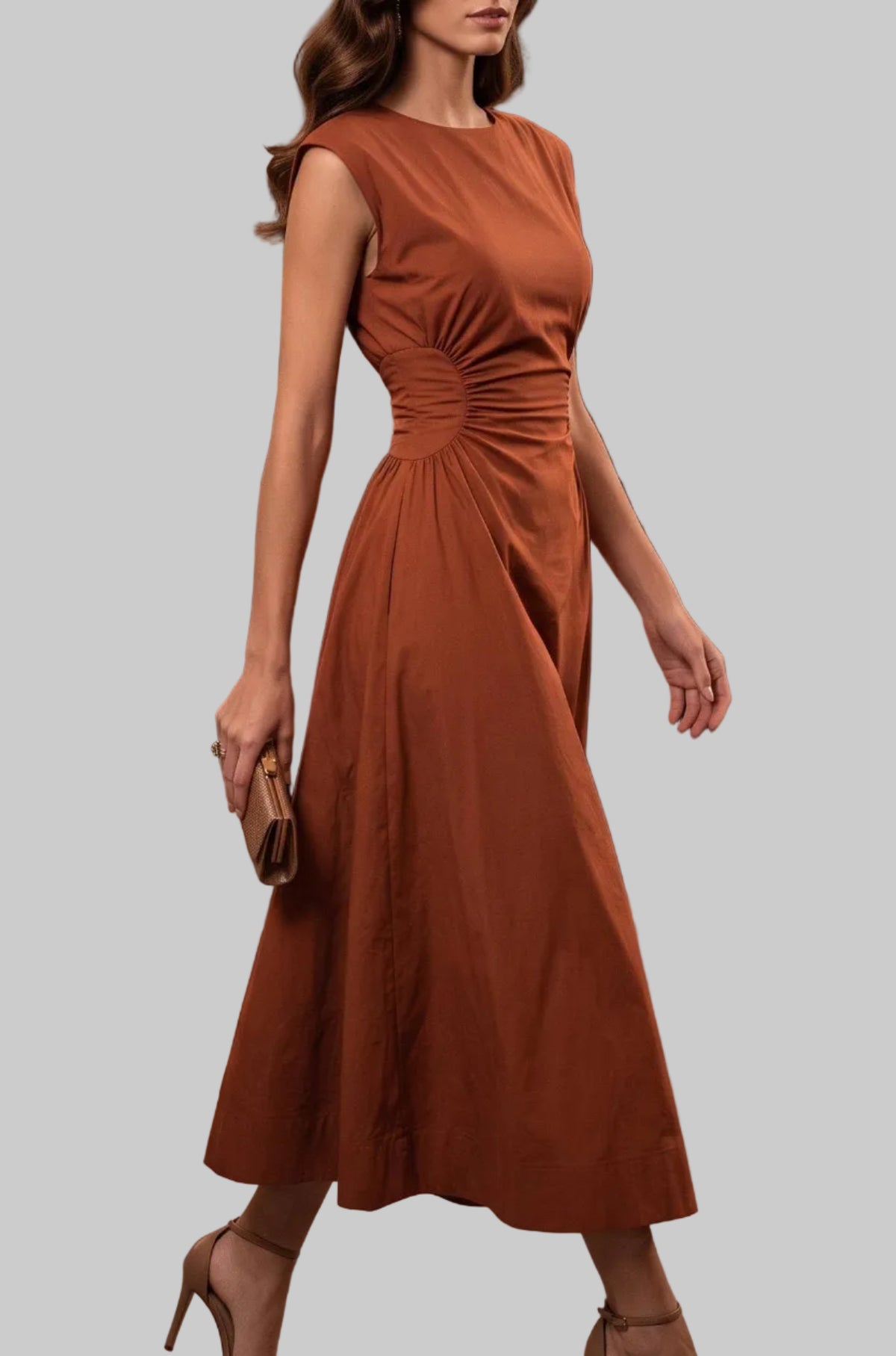 A woman wearing a sleeveless rust-orange midi dress with a gathered waist and nude high heels, walking in a dimly lit event venue with guests blurred in the background.
