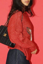Person wearing a red sweater with a black handbag against a pink background