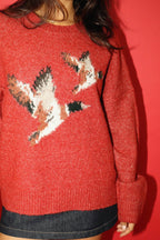 Red sweater with bird pattern worn by a person against a red background