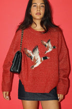 Woman wearing a red sweater with a mallard design against a pink background