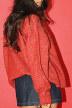 Person wearing a red sweater and denim shorts against a pink background