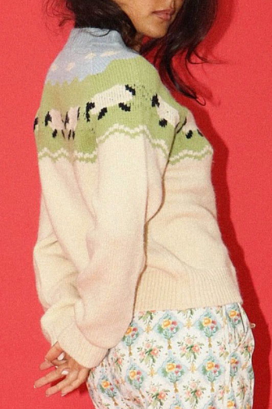 Person wearing a cream sweater with a colorful pattern on a red background