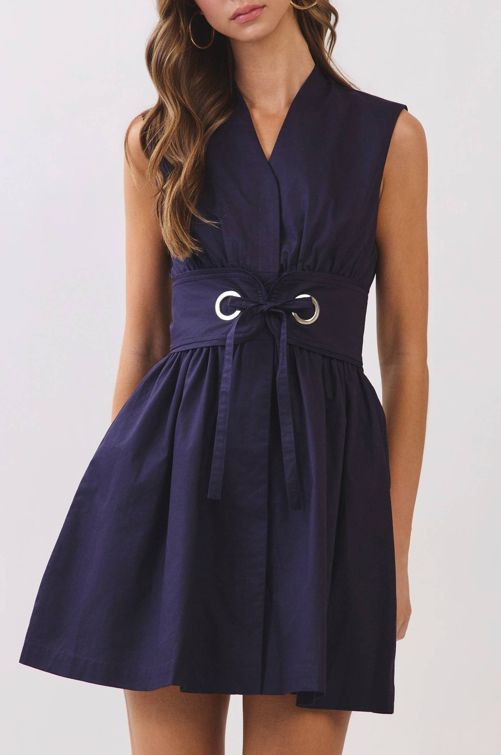 Woman wearing a navy sleeveless dress with a belt on a white background
