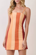 A woman modeling a sleeveless mini dress with vertical color-blocked stripes in peach, orange, and rust red on a light beige studio background.
