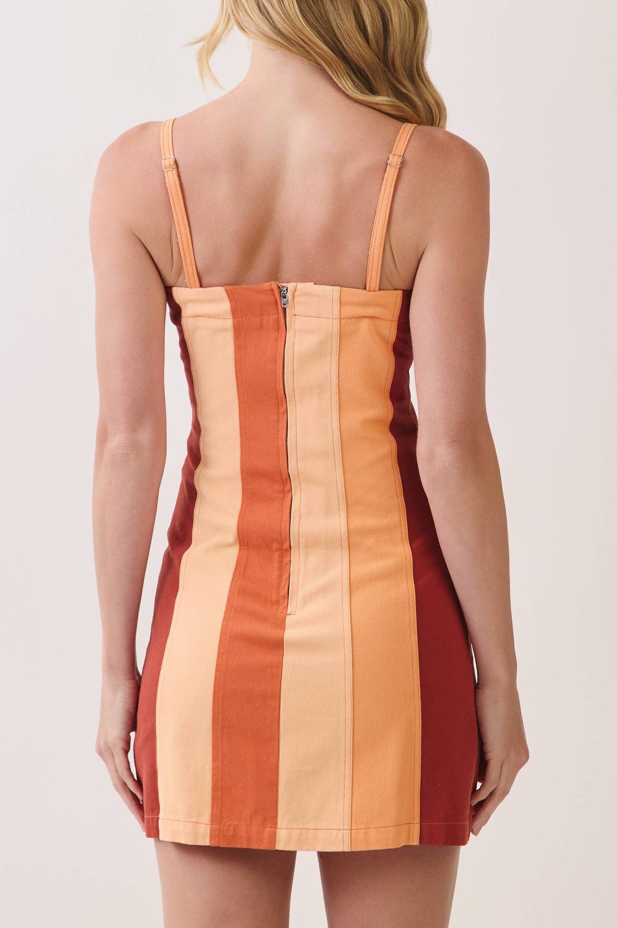 A woman shown from the back wearing a sleeveless mini dress with vertical stripes in peach, orange, and deep red, against a plain light background.