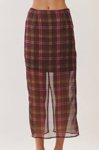 A model wearing a brown and red plaid midi skirt with a sheer front slit, paired with beige heeled sandals, against a plain light background.