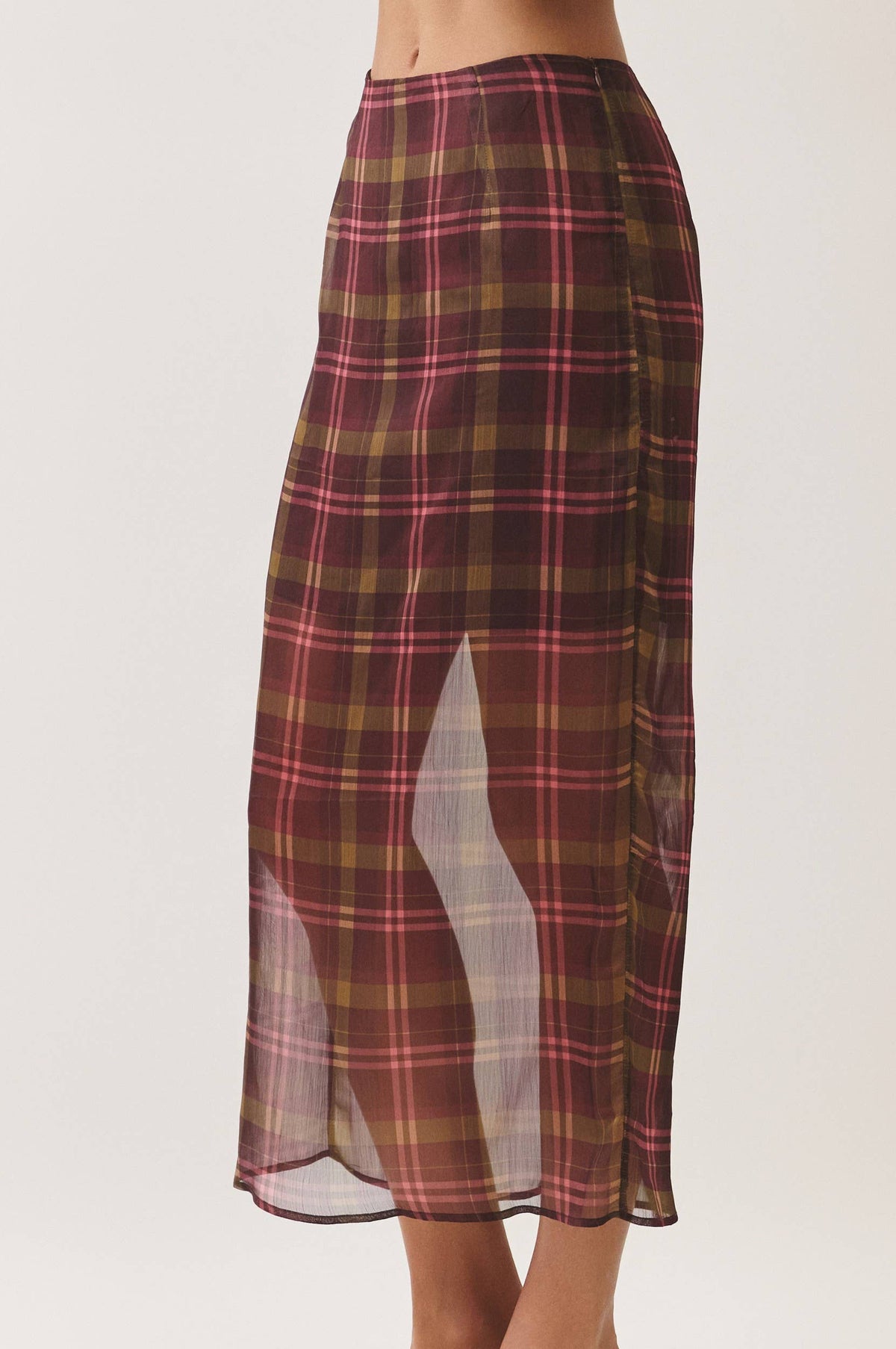 A model wearing a mid-calf plaid skirt in burgundy, brown, and pink, paired with beige block-heel sandals, shown from the waist down against a light gray studio background.