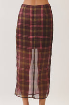 A woman's midi skirt with a sheer overlay and a front slit, featuring a brown, red, and gold plaid pattern. The model is shown from the back wearing beige block-heel sandals against a plain light beige studio background.