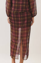 A woman viewed from the back wearing a sheer long-sleeve plaid shirt and matching midi skirt set. The fabric has a brown and burgundy base with thin pink and yellow lines in the plaid pattern, set against a plain light beige studio background.