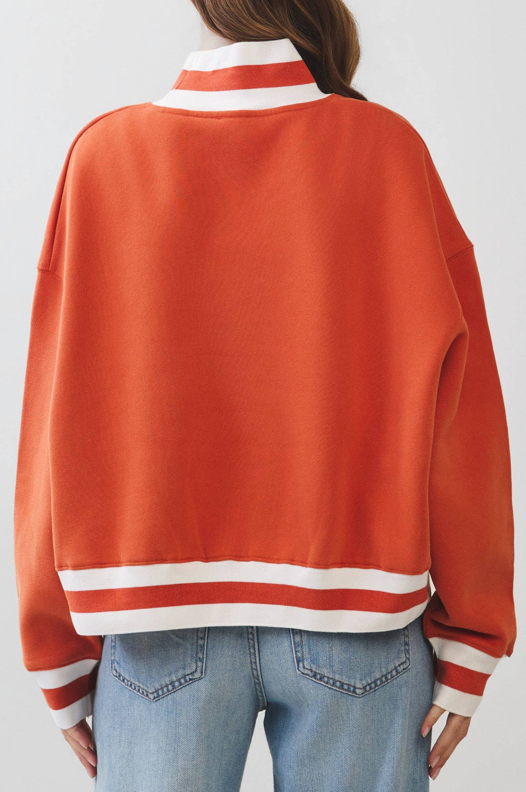 Person wearing an orange varsity jacket with white stripes on a plain background
