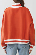 Person wearing an orange varsity jacket with white stripes on a plain background