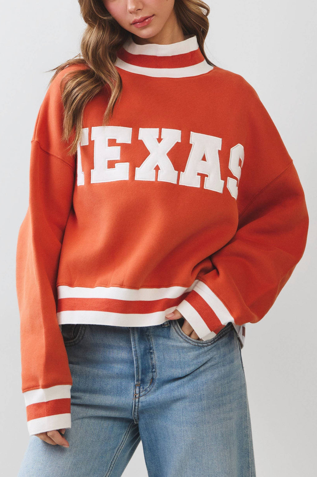 Person wearing a red 'TEXAS' sweater with blue jeans on a plain background