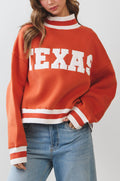 Person wearing a red 'TEXAS' sweater with blue jeans on a plain background