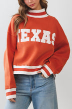 Person wearing a red 'TEXAS' sweater with blue jeans on a plain background