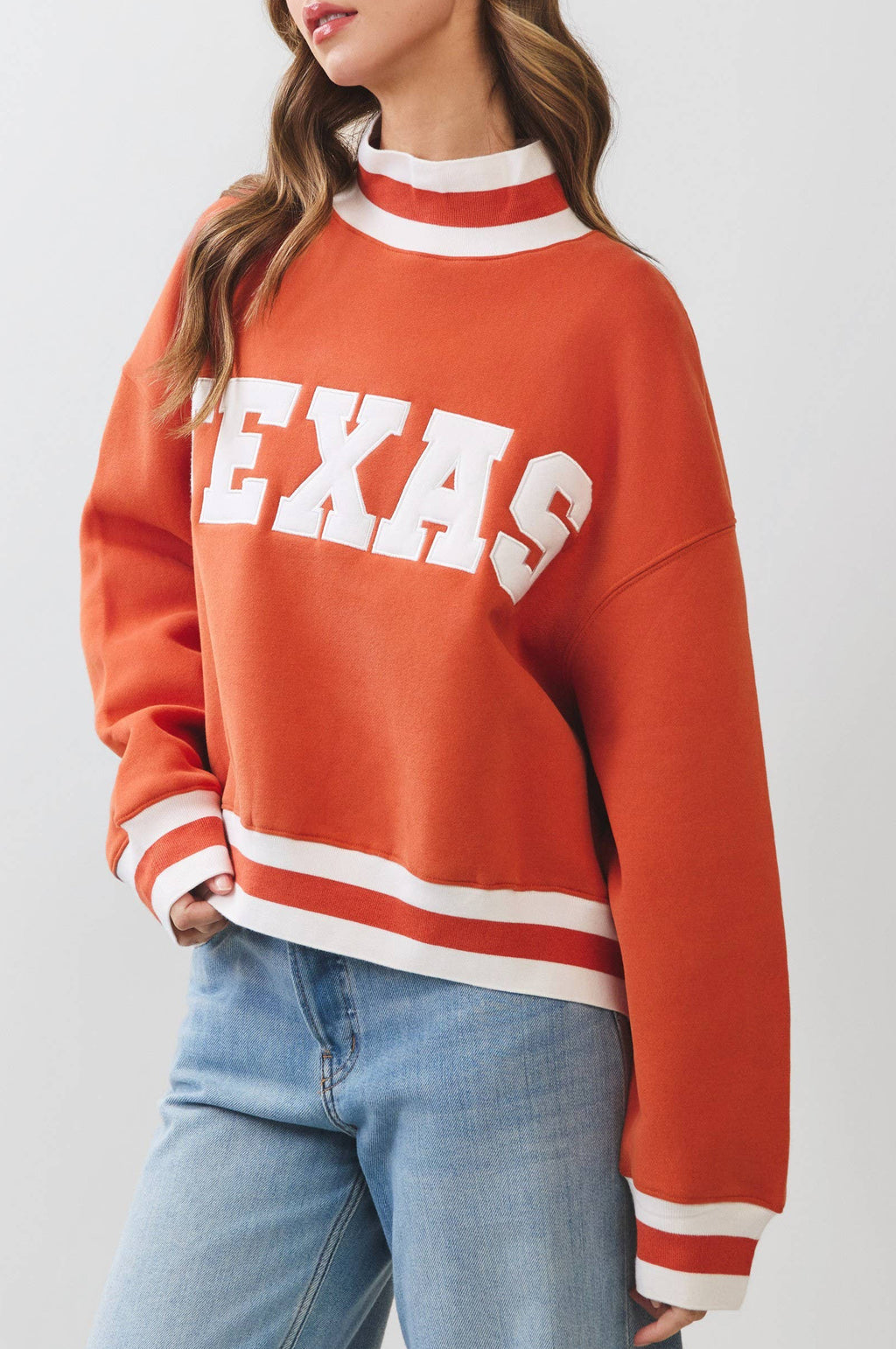 Person wearing an orange 'TEXAS' sweatshirt with white stripes on a plain background