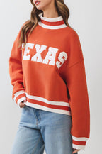 Person wearing an orange 'TEXAS' sweatshirt with white stripes on a plain background