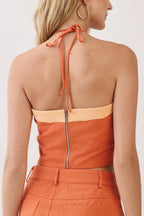A woman shown from the back wearing a bright orange halter mini dress with beige contrast trim and a central zipper, photographed against a plain light background.