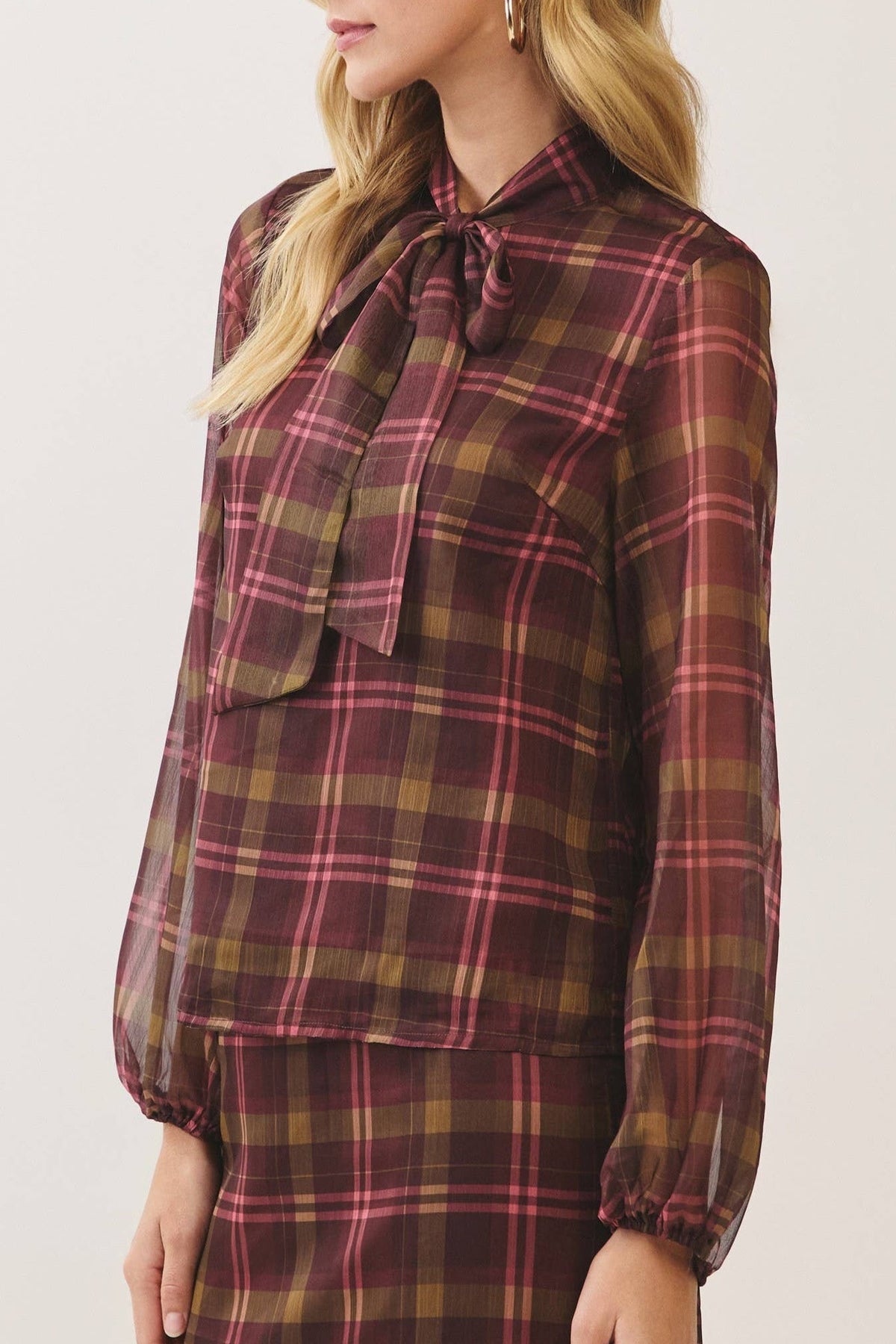 A woman modeling a matching plaid long-sleeve blouse and skirt set. The fabric features a classic tartan pattern in deep burgundy, brown, and muted green.