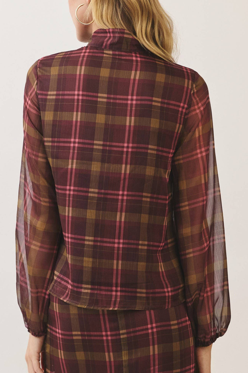 A woman shown from the back wearing a matching plaid long-sleeve top and skirt set. The fabric features a classic tartan pattern in dark red, brown, and yellow with thin pink stripes, set against a plain off-white studio background.