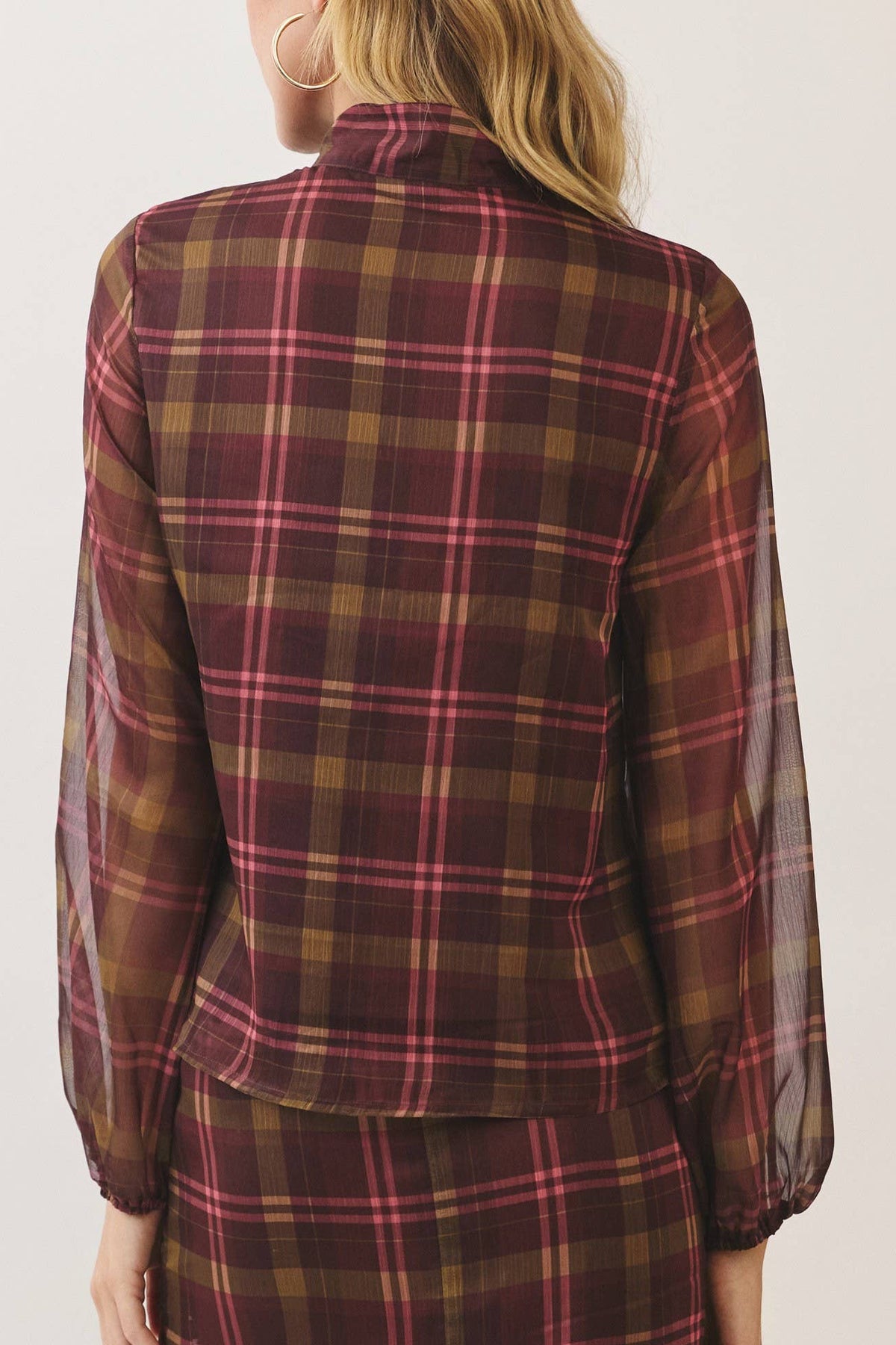 A woman shown from the back wearing a matching plaid long-sleeve top and skirt set. The fabric features a classic tartan pattern in dark red, brown, and yellow with thin pink stripes, set against a plain off-white studio background.