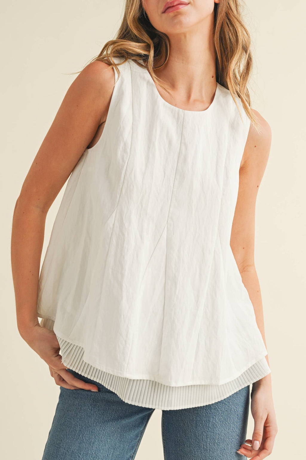 Woman wearing a white sleeveless top and blue jeans against a beige background