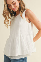 Woman wearing a white sleeveless top and blue jeans on a beige background