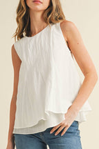 Woman wearing a white sleeveless top and blue jeans on a beige background