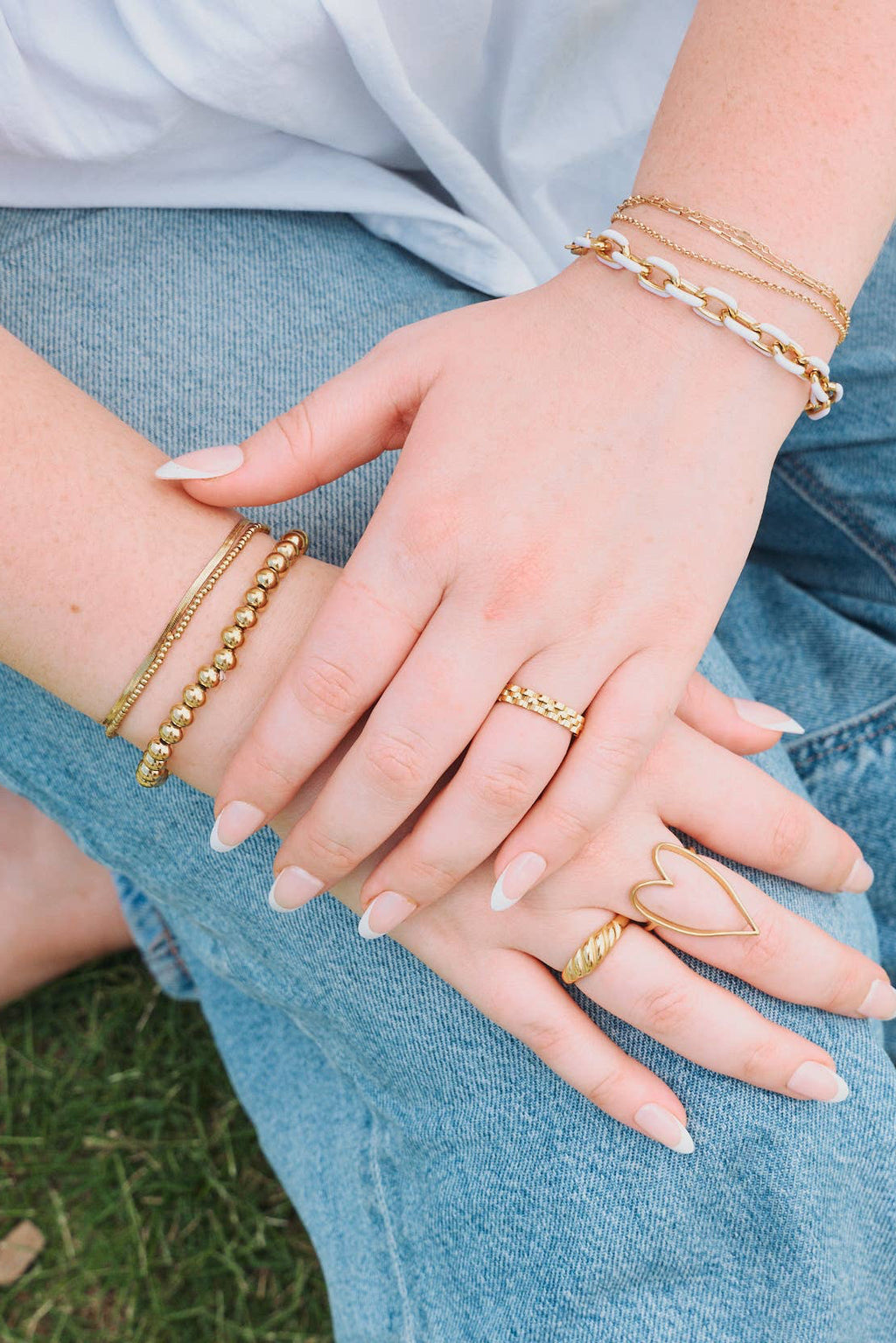 Person wearing gold bracelets and rings on a grassy background