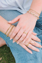 Person wearing gold bracelets and rings on a grassy background