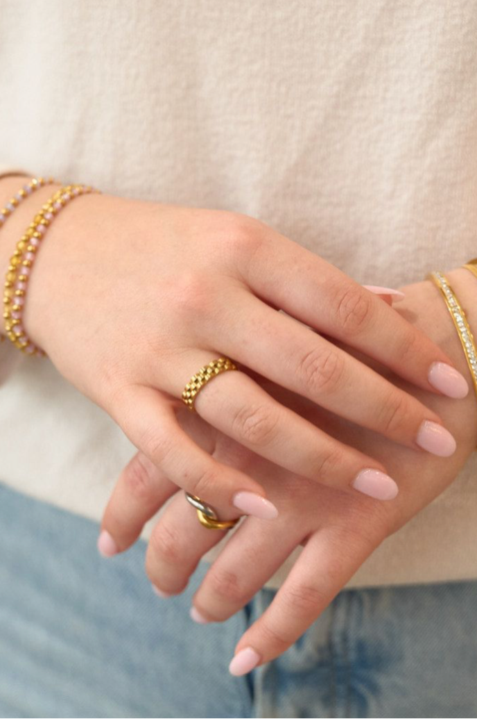Close-up of a person's hands wearing gold bracelets and rings against a neutral background