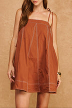 Woman wearing a rust-colored dress with thin straps against a beige background