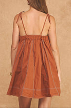 Woman wearing a rust-colored dress with thin straps against a beige background