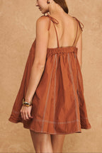 Woman wearing a rust-colored dress with thin straps against a beige background