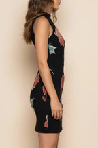 Woman wearing a black dress with colorful patterns against a beige background