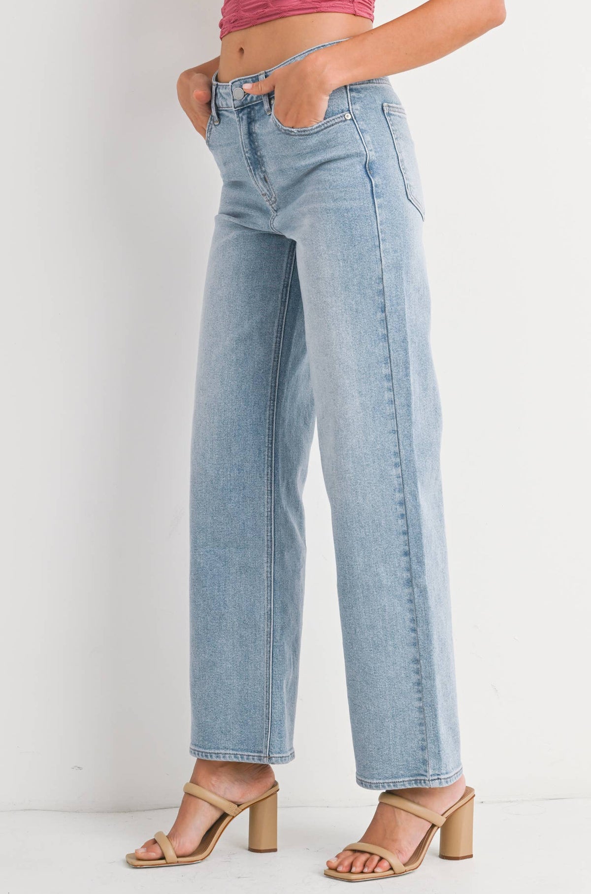 Woman wearing a pink halter top and light blue jeans on a white background