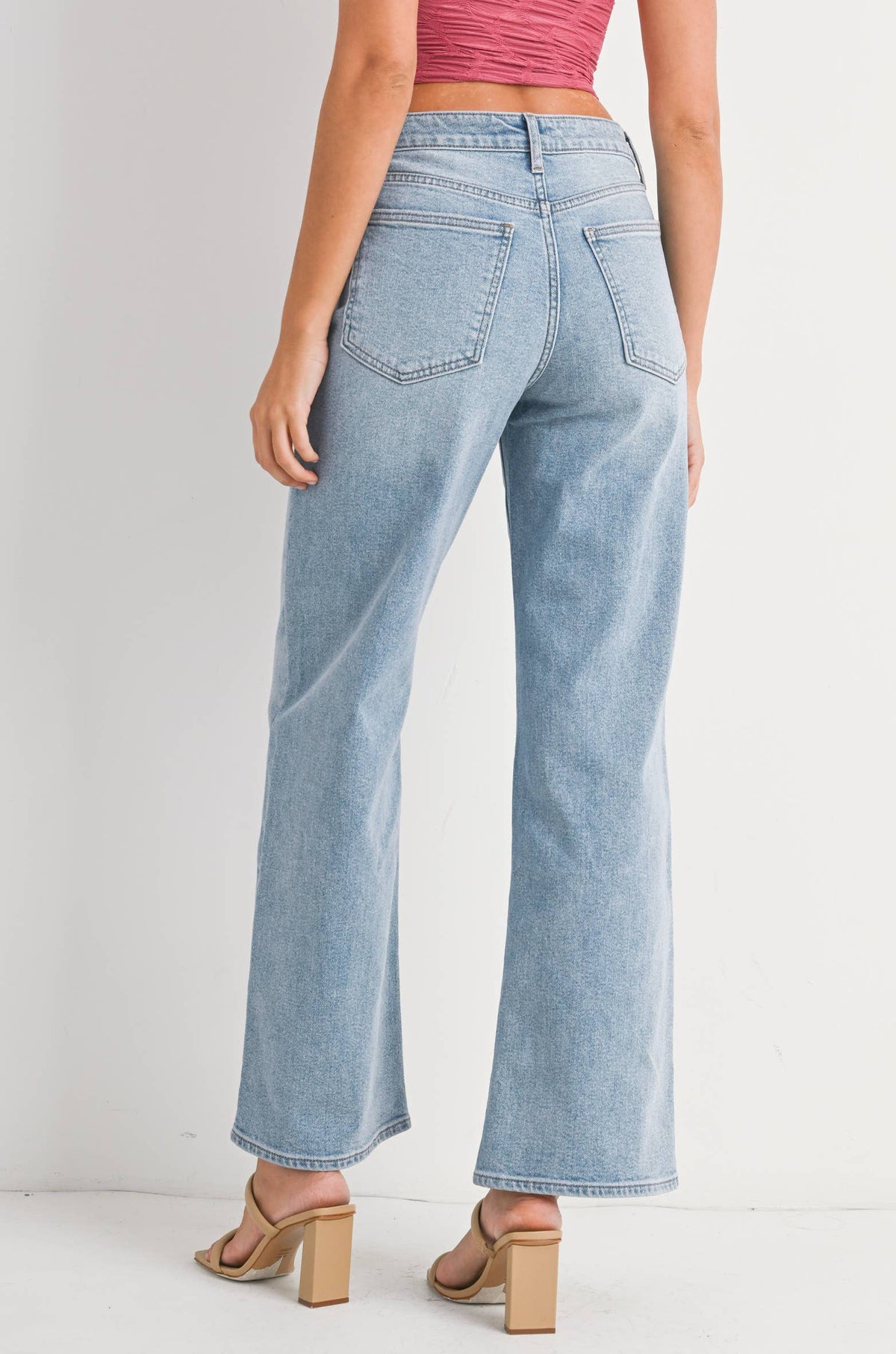 Woman wearing light blue jeans and a pink top on a white background