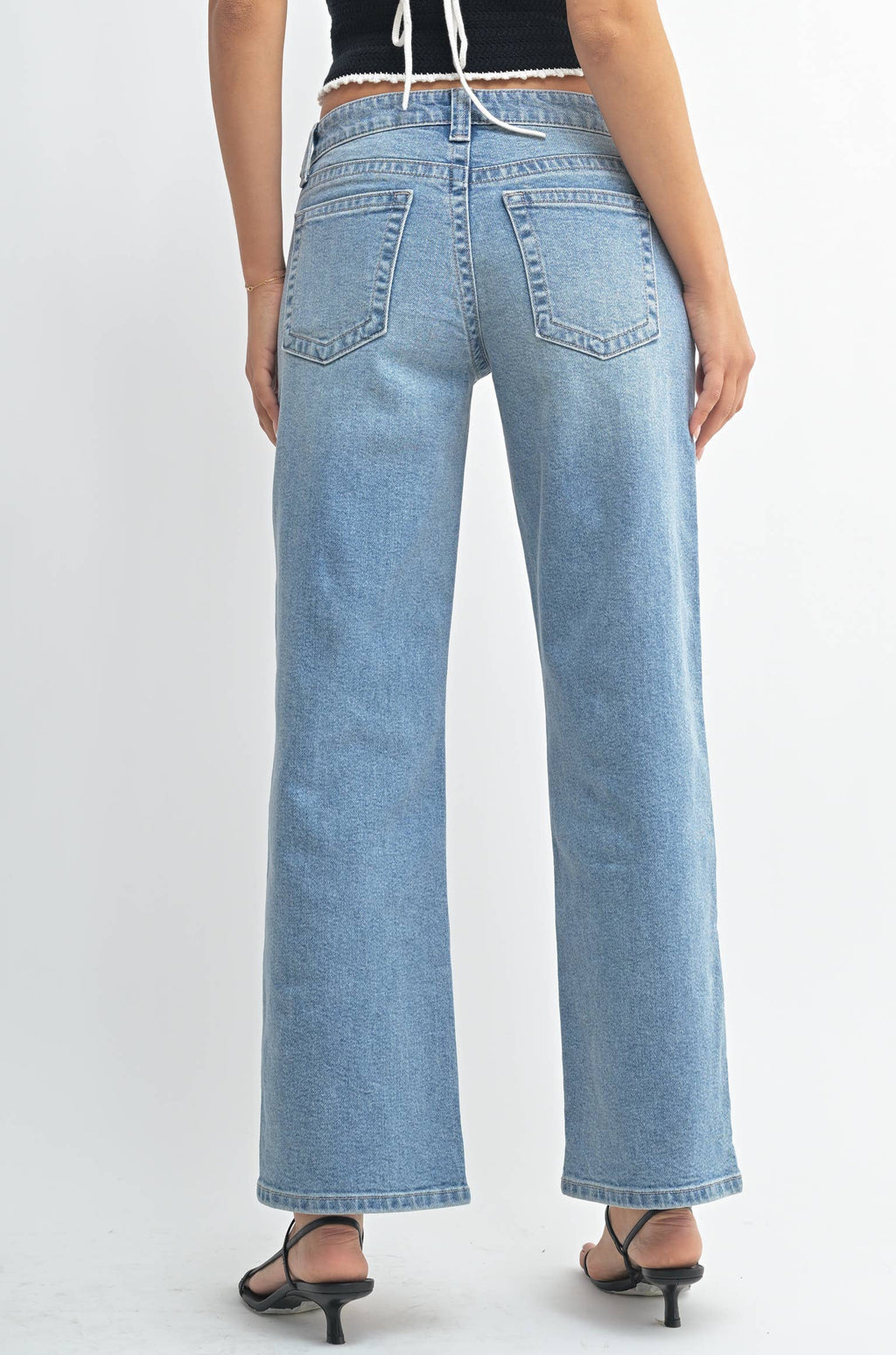 Woman wearing a black strappy top and light blue jeans on a white background