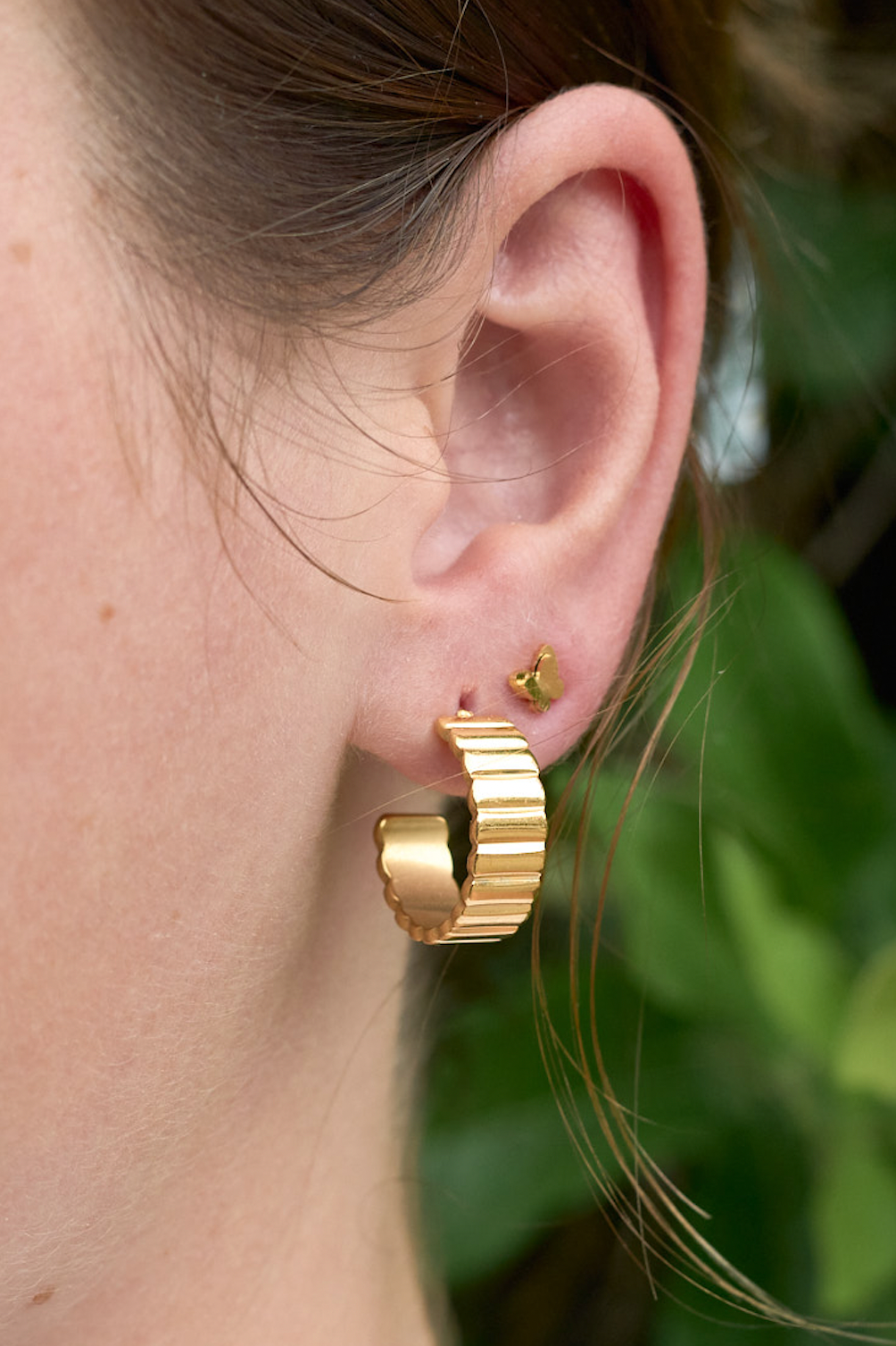 Close-up of a person wearing gold hoop earrings with a blurred green background