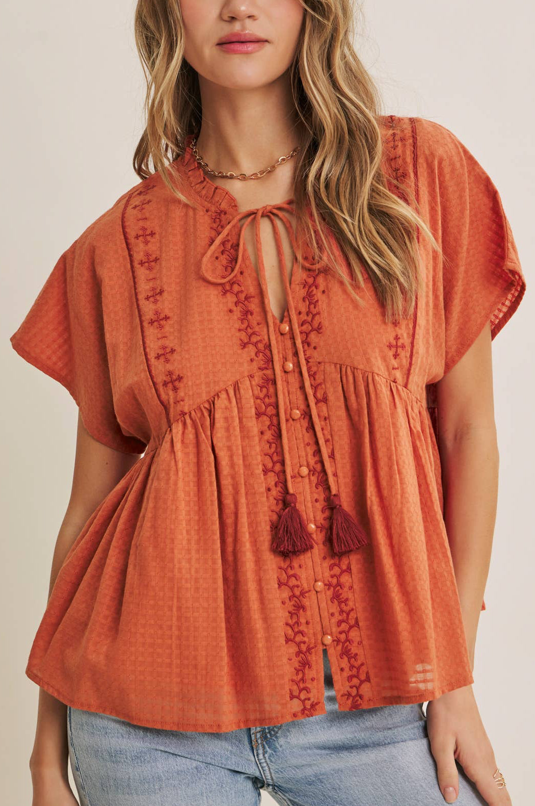 Woman wearing an orange embroidered blouse with a plain background
