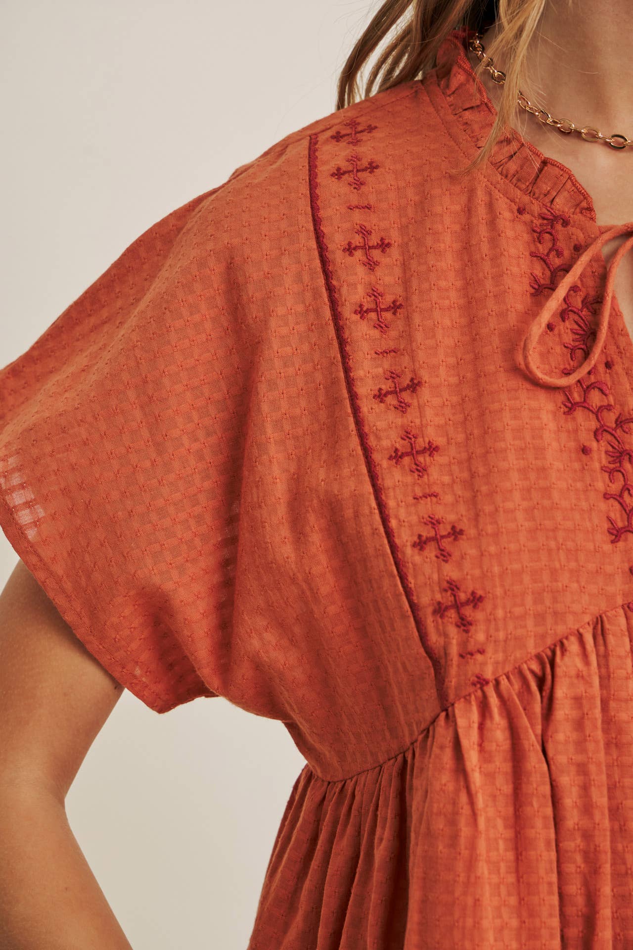 Close-up of a rust-colored dress with intricate embroidery on a neutral background