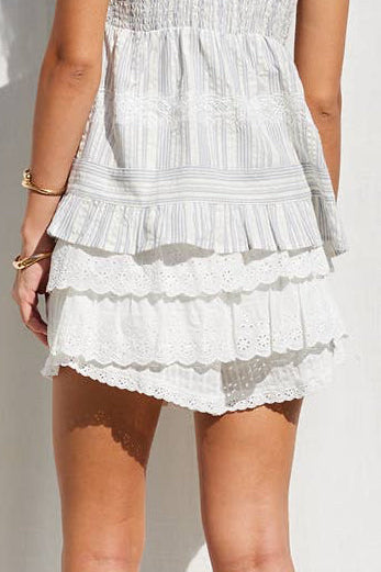 Woman wearing a white tiered dress standing against a white curtain.